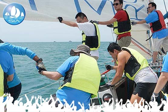 corporate team sailing members working as a crew to raise the mainsail on a sail in asia yacht
