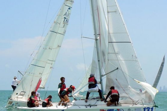 sailing crew working closely together rasing mainsail on a racing yacht during a corporate sailing regatta with sail in asia